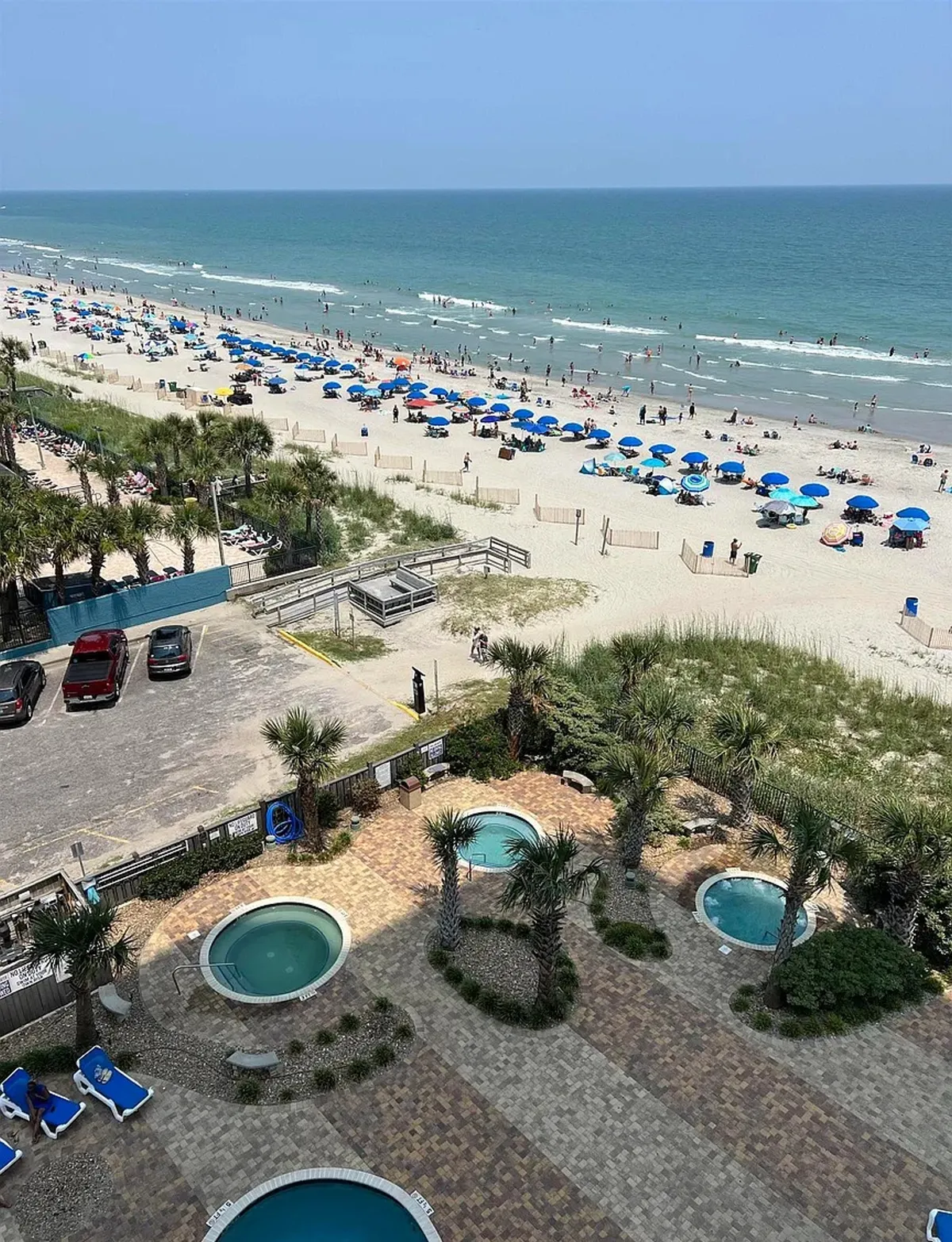 An exterior view presents the resort's beachfront amenities, including swimming pools, palm trees, umbrellas, and direct access to the sandy beach and ocean waves. Guests can be seen enjoying various leisure activities, enhancing the sense of community and resort lifestyle.
