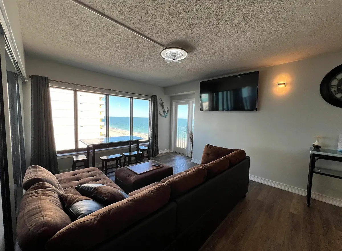 This image features a cozy living area with a comfortable couch, a dining table, and large windows providing a clear ocean view. The space feels inviting and warm, ideal for relaxing after a day at the shore or enjoying a meal with the backdrop of the sea.