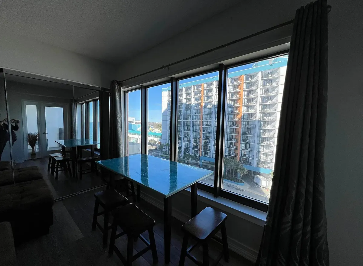 A tranquil dining area within the condo, featuring large windows that open up to beautiful sunrise views over the ocean. A mirrored wall enhances the sense of space and light, while the dining table is perfectly positioned for couples to enjoy a meal together with the view as a backdrop.
