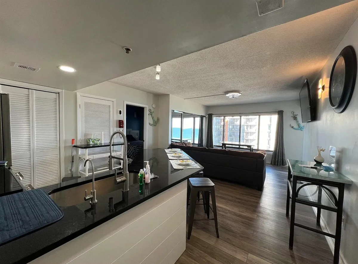 An airy kitchen and dining area featuring a kitchen island, large windows letting in natural light, a comfortable sofa, and a dining table. The open layout encourages both cooking and socializing, with inviting views and a contemporary feel.
