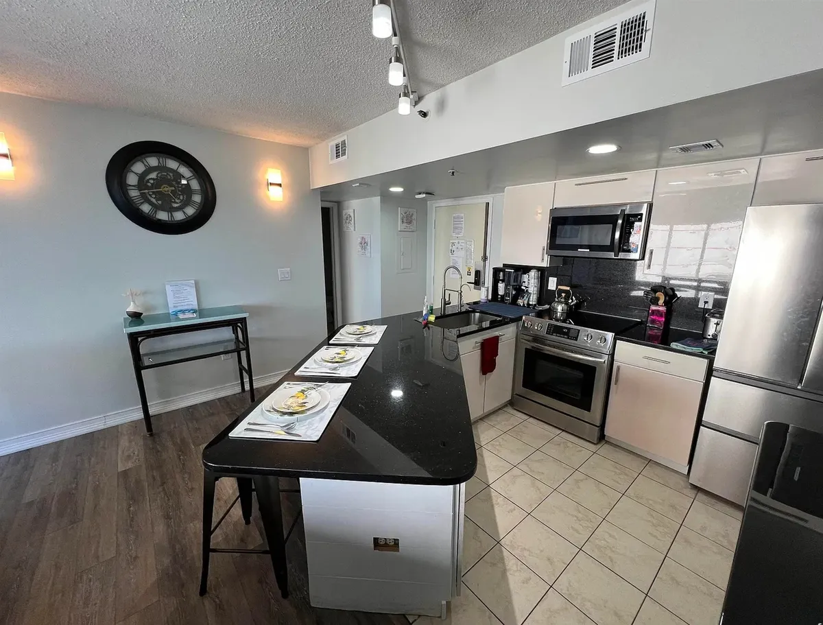 This image highlights a modern kitchen with a central island, stainless steel appliances, a wall clock, and decorative elements on the countertops. The setup invites guests to cook, entertain, and enjoy family meals in a welcoming, well-equipped space.