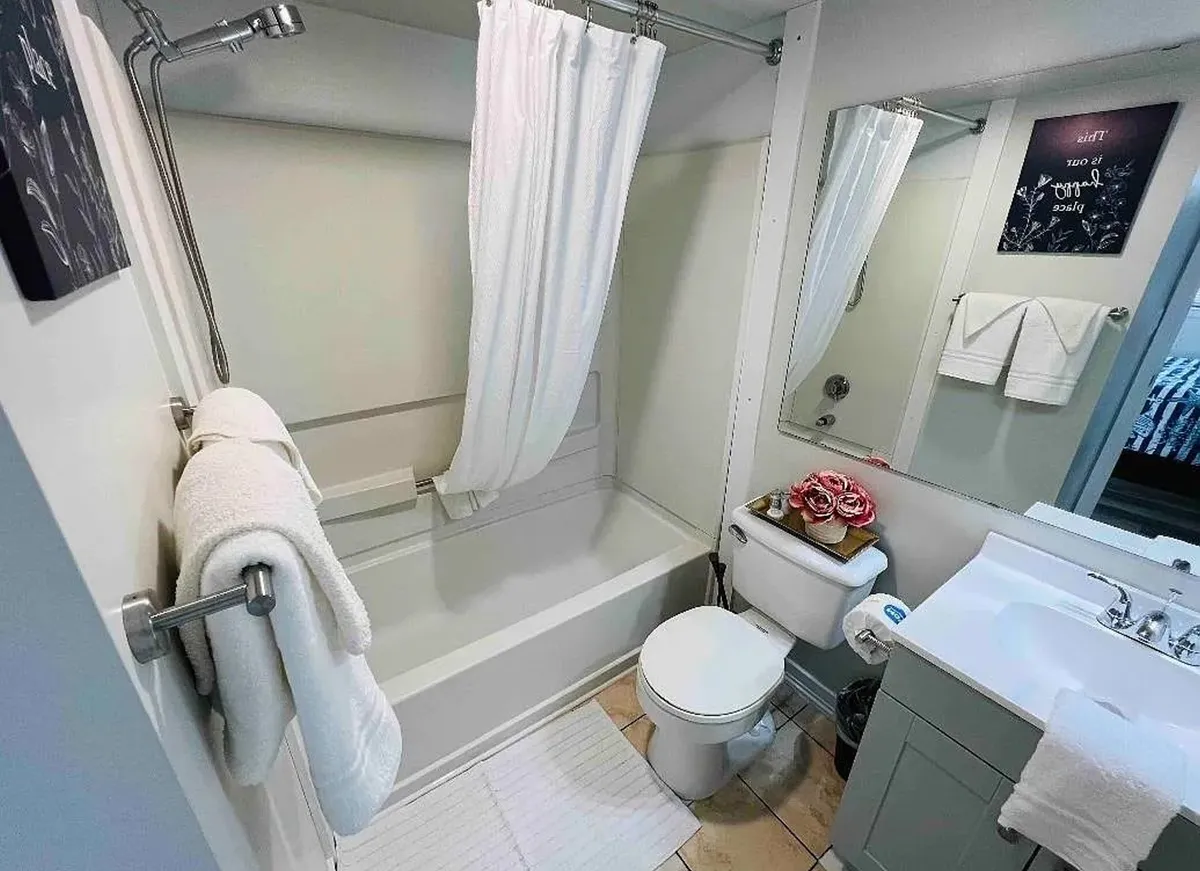 A modern bathroom with a bathtub, mirror, sink, plush towels, and decorative flowers. The setting is serene, organized, and designed for relaxation and self-care routines.