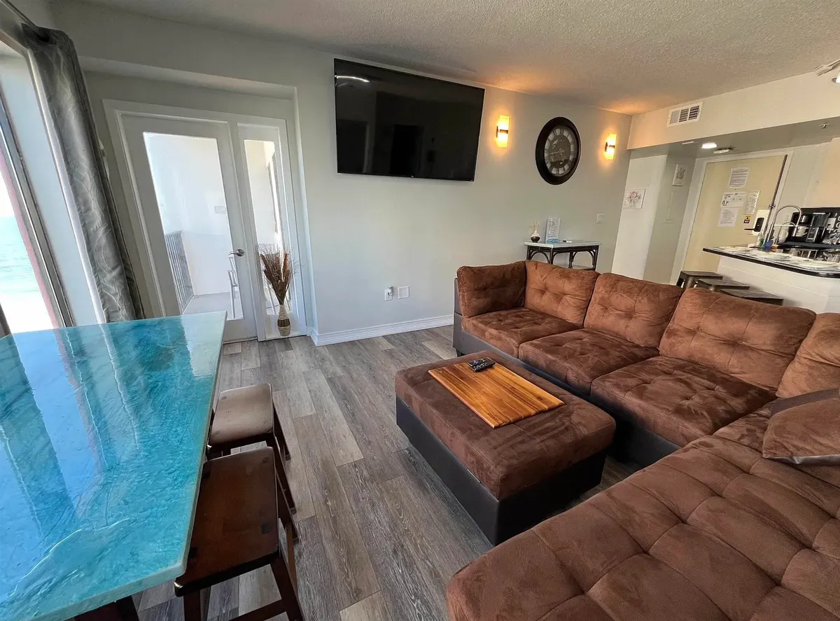 A cozy living room with a plush sofa, coffee table, and a bar area, arranged to face large windows that offer sunset views. The space encourages relaxation, intimate movie nights, or enjoying a toast together while watching the landscape change outside.